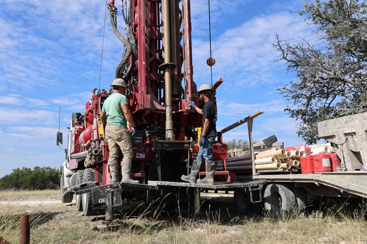 Triangle J Water Wells crew drilling a water well from their red rotary rig under a blue North Texas sky